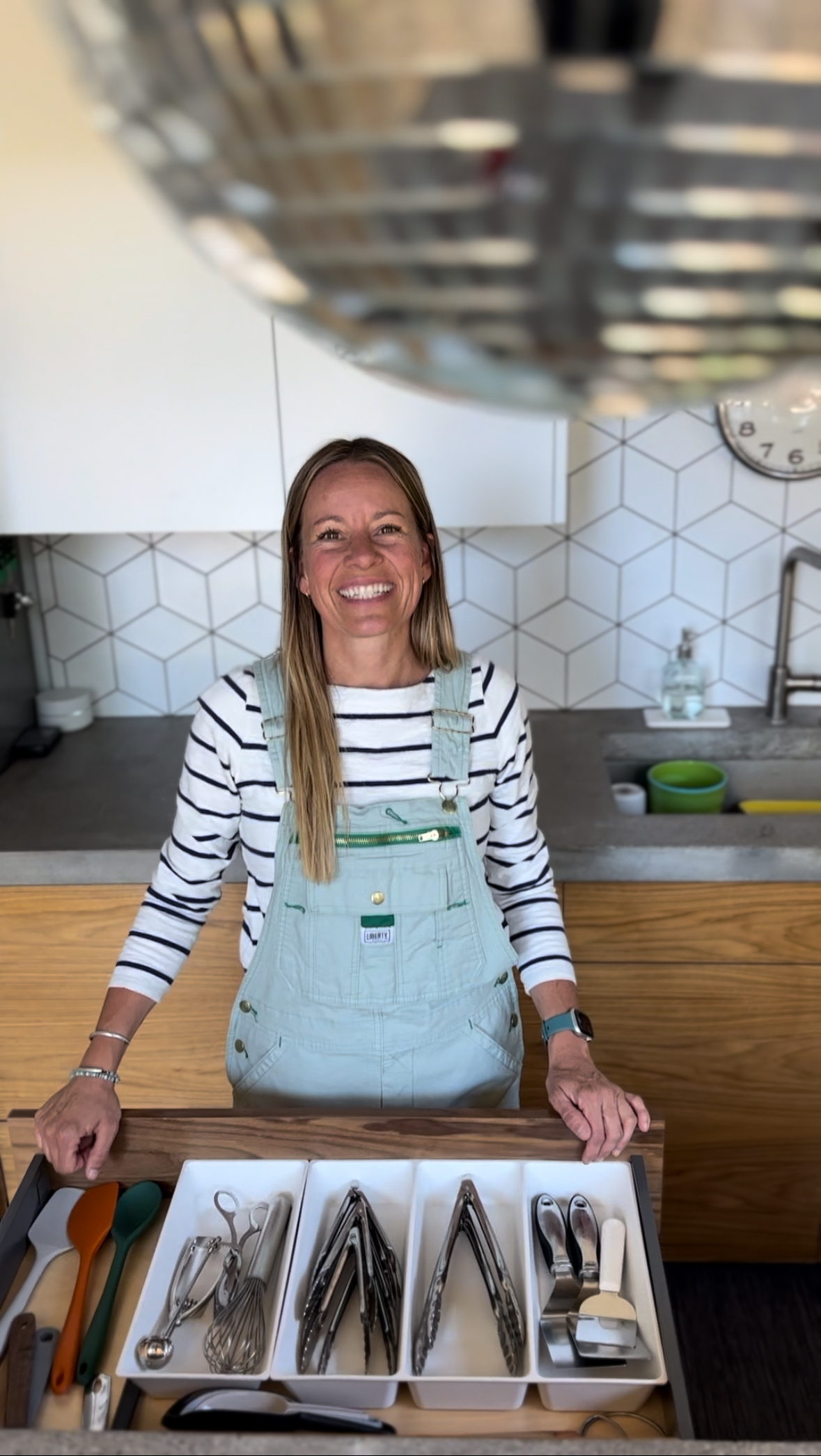 A woman in a clean, organized kitchen showing a clean silverware drawer with a drawer organizer