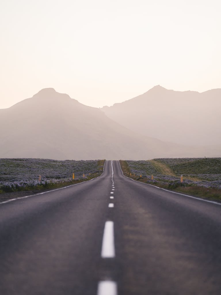 A picturesque view of an empty road leading towards distant mountains under a soft dawn sky in Iceland.